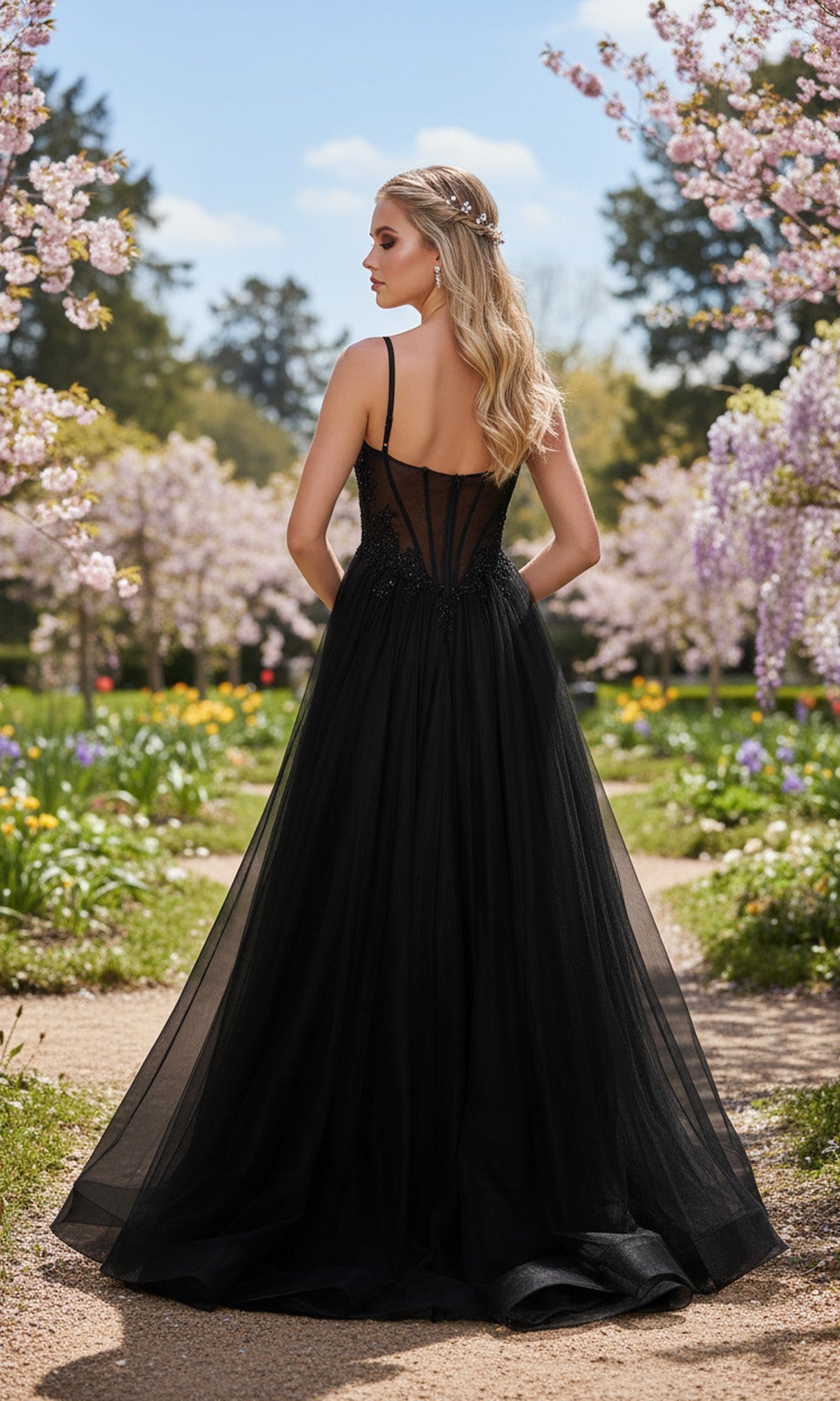 A woman wearing the La Femme 33436 long prom dress with a black high-slit a-line skirt and embellished corset bodice stands on a garden path among blooming trees and flowers, facing away from the camera.